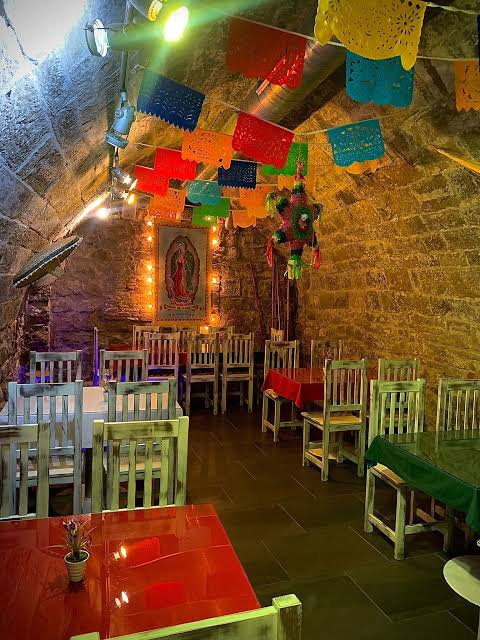 Planta inferior con bóveda de piedra, papel picado y mesas de colores